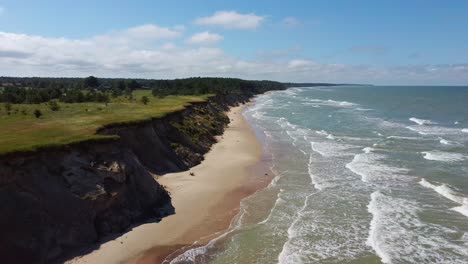 Flying-Over-Coastline-Baltic-Sea-Ulmale-Seashore-Bluffs-Near-Pavilosta-Latvia-and-Landslides-With-an-Overgrown,-Rippling-Cave-Dotted-Cliff-and-Pebbles