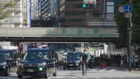 Stream-Of-Taxis-And-UberEat-Cyclist-Passing-By-Shibuya-Crossing-During-The-Pandemic-With-No-Tourists-In-Tokyo,-Japan