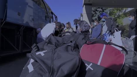 1-4-Aufgestapelte-Gepäck-Hockeytaschen-Neben-Der-Busaufbewahrung-Mit-überfüllten-Maskierten-Passagieren-Missachten-Das-2-Meter-6-Fuß-Gesetz-Zur-Physischen-Sozialen-Distanzierung,-Während-Das-Personal-Unmaskiert-Reisenden-Beim-Gepäck-Hilft