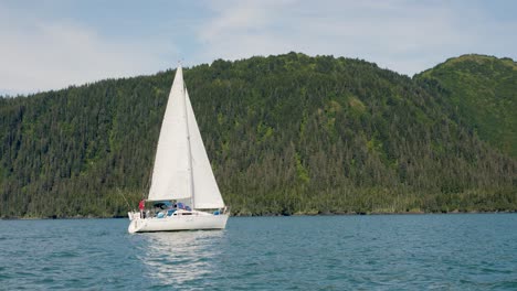 Tourists-On-Sailboat-Sailing-In-The-Ocean-With-Forested-Mountain-In-Background-In-Alaska