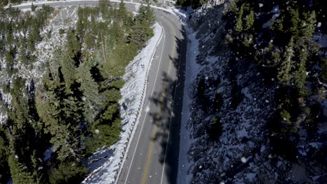 Nevando-Sobre-Una-Carretera-Curva-Vacía-En-Las-Montañas-Y-árboles-Cubiertos-De-Nieve