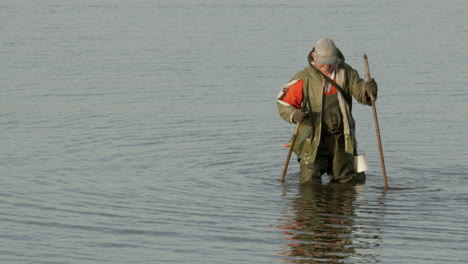 Old-fisherman-with-fishing-equipment-walking-through-water-during-sunny-day