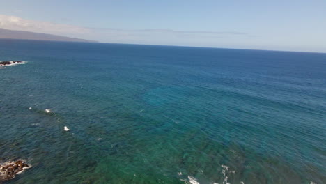 Standing-in-wonder-on-cliff-above-blue-ocean,-aerial-into-azure-water,-Maui