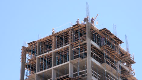 Construction-Builders-Lowering-Bucket-from-Top-of-Building-Site,-Low-Angle