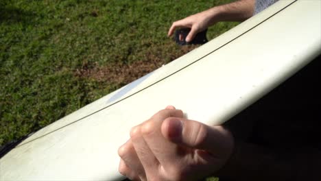 Detail-of-the-hands-of-a-surfer-removing-wax-from-the-board