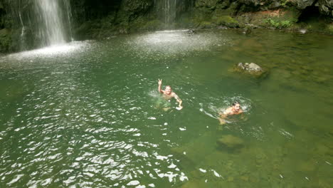 Two-male-hikers-swim-and-relax-in-pool-by-Waikani-Falls-on-Road-to-Hana,-Maui