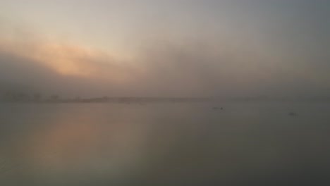 Ghostly-mist-during-sunrise-above-peaceful-Frydman-Lake,-aerial