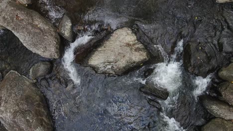Hoher-Blick-Auf-Ein-Natürliches-Bachbett-Mit-Wasser,-Das-Zwischen-Farbigen-Felsen-Fließt