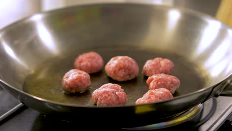 Small-size-juicy-meat-balls-frying-in-a-steel-pan-with-hot-olive-oil,-handheld-close-up-shot
