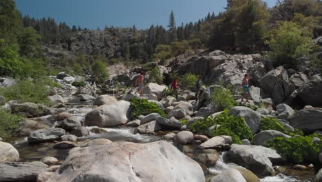 Four-young-men-in-swim-trunks-cross-Yuba-River-on-rocky-boulders