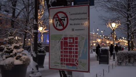 People-walking-behind-a-No-Drone-zone-sign-in-Helsinki,-Finland-in-Esplanadi-park