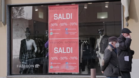 Gente-Caminando-Frente-A-Un-Escaparate-De-Ropa-De-Mujer-Con-Afiche-Rojo-De-Ventas