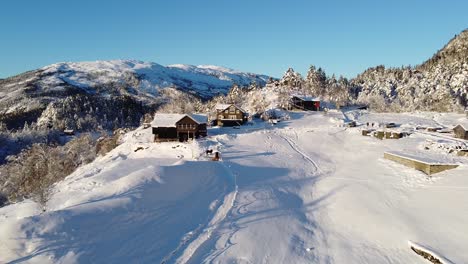 Toma-Aérea-Sobre-Una-Granja-Cubierta-De-Nieve-En-Las-Montañas-De-Noruega---Escena-De-Invierno