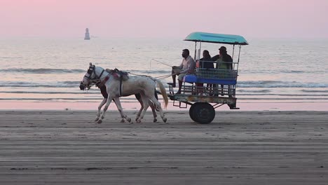 Eine-Kleine-Asiatische-Familie,-Die-Am-Strand-In-Einem-Pferdewagen-Reitet-Und-Ferien-Genießt,-Ein-Pferdewagen-Am-Strand-Bei-Sonnenuntergang-Mit-Einer-Kleinen-Gruppe-Von-Menschen-Darin