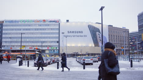 Toma-En-Cámara-Lenta-De-Personas-Caminando-Por-Un-Gran-Anuncio-De-Samsung-En-La-Nevada-Helsinki