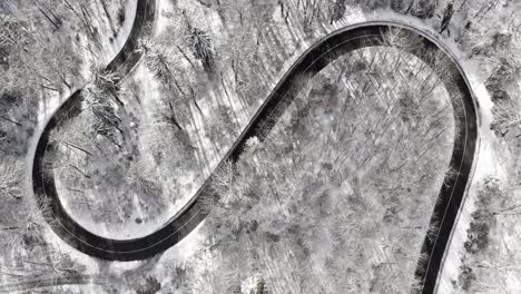 Double-bending-s-curve-in-a-snowy-woodland-landscape,-captured-straight-from-above