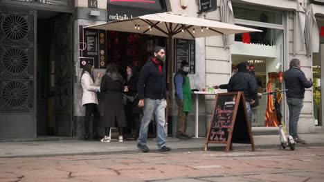 Hipster-Man-In-Mask-Comes-Out-Of-A-Bar-Showing-A-Peace-Sign,-Facing-The-Camera-And-Walks-Away