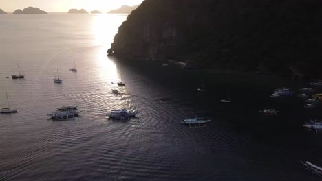 4K-Aerial-Drone-Shot-of-Tour-and-Fishing-Boats-in-the-Bay-During-Sunset-at-Corong-Corong-Beach-in-El-Nido,-Palawan,-Philippines