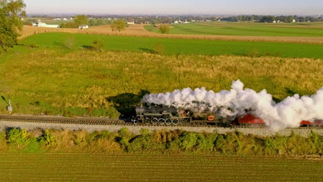 Aerial-View-of-Farmlands-at-Sunrise-with-a-Steam-Engine-and-Passenger-Train-Traveling-with-a-Full-Head-of-Steam-and-Smoke