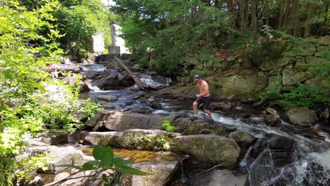 Young-Caucasian-topless-man-crossing-river-in-the-forest-on-e-sunny-summer-day