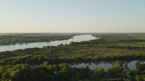 Aerial-parallax-of-Zarate-large-green-fields-and-forest-area-and-Parana-river-flowing-into-horizon-at-golden-hour,-Entre-Rios,-Argentina