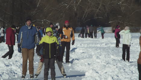 Large-group-of-people-happily-ice-skating-enjoying-a-sunny-holiday-in-Lhotka-Frozen-lake-in-Kokorin,-Czech-Republic---Medium-slow-motion-static-shot