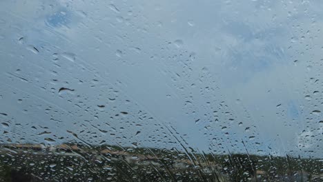 closeup-of-Raindrops-falling-on-car-windsield-and-window-with-houses-and-clouds-in-the-background
