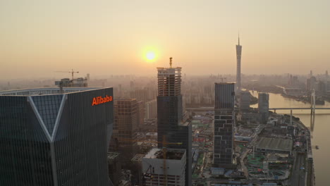 Fly-over-construction-site-of-Alibaba-Group-office-bulding-district-on-bank-of-Pearl-river-at-colorful-golden-sunset-with-Canton-tower-in-far-distance