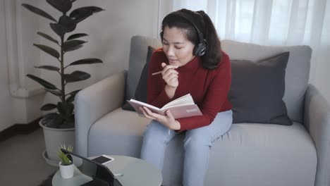 Businesswoman-redshirt-using-a-tablet-with-headphone-for-meeting-online-at-home
