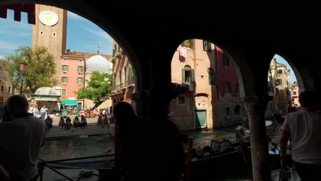 Slow-motion-shot-showing-silhouette-of-tourists-walking-along-promenade-beside-canal-in-Venice