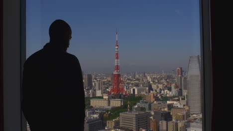 Silhouette-Eines-Erwachsenen-Mannes,-Der-Aus-Dem-Hotelfenster-Mit-Blick-Auf-Tokio-Schaut
