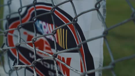 NASCAR-flag-waving-behind-a-chain-link-fence,-handheld-close-up