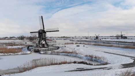Snow-covered-Dutch-windmills-canals-and-polder-land,-cold-winter-aerial-view