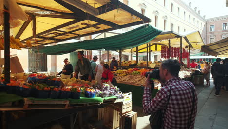 Slow-motion-dolly-shot-of-male-photographer-taking-pictures-of-woman-buying-fresh-fruits-and-vegetables-on-Venetian-street-market-during-sunlight