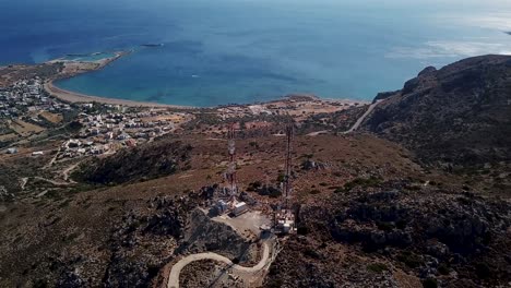 Right-trucking-rotating-drone-shot-of-rural-cellular-towers-above-a-mountain-landscape-revealing-the-town-and-Mediterranean-sea