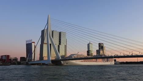 Skyline-of-Rotterdam-seen-from-the-river-Maas-with-the-Erasmus-bridge-and-high-rise-buildings-of-the-financial-district-and-docked-MSC-Preziosa-cruise-ship-against-a-clear-blue-sky-at-sunset