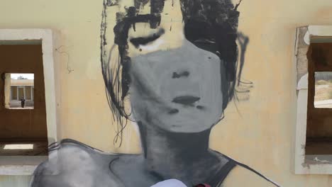 man-graffiti-painting-a-woman-face-on-an-yellow-building-wall,-isolated-place,-close-up