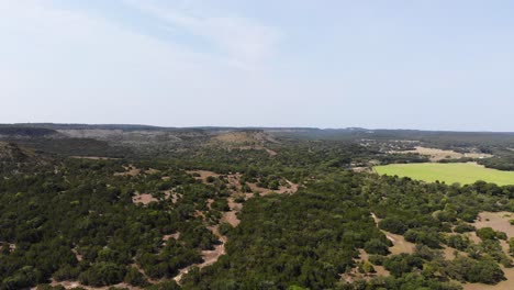 Slowly-descending-above-gorgeous-view-of-the-Texas-hill-country-with-vivid-blue-sky-and-green-field,-many-hills,-trails,-trees
