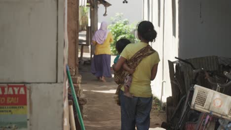 Asiatische-Mutter-Mit-Einem-Kind-Auf-Dem-Arm-In-Einer-Kleinen-Gasse-Auf-Einer-Tropischen-Insel-In-Lombok,-Indonesien