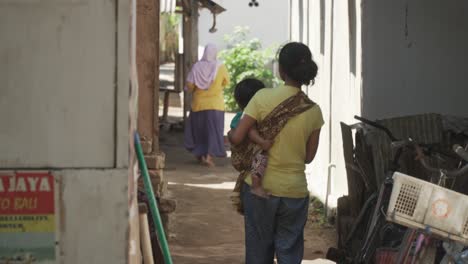 Asian-mother-with-a-child-on-her-arm-in-a-small-alley-on-a-tropical-island-in-Lombok,-Indonesia