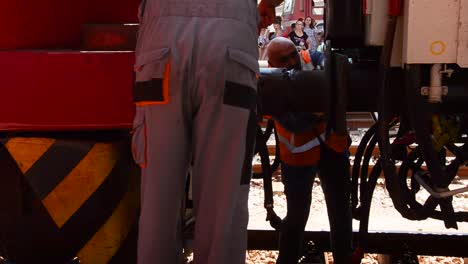 Bulgarian-railway-workers-wearing-orange-hi-vis-safety-workwear,coupling-a-locomotive-engine-train-to-carriages-with-passengers-waiting-on-background-platform