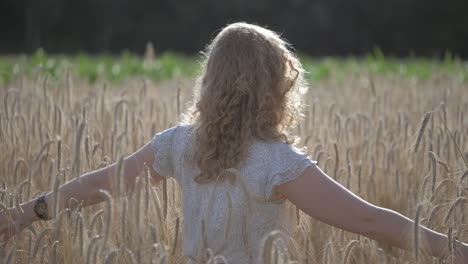 Young-woman-spinning-and-smiling-in-a-wheat-field,-on-a-sunny-evening
