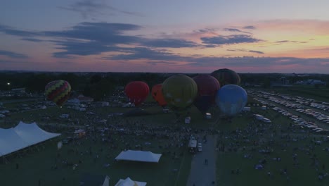 Vista-Aérea-De-Globos-Aerostáticos-Llenándose-Para-Un-Espectáculo-Nocturno-De-Llamas-En-Un-Festival-De-Globos-Al-Atardecer-Visto-Por-Un-Dron