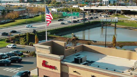 Aerial-tilt-up-reveals-Chick-fil-A-fast-food,-American-flag,-busy-highways