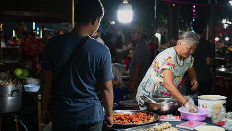 Fish-ball-and-sausage-deep-fry-vendor-packing-for-buying-customer-at-the-Thai-night-market-receiving-payment