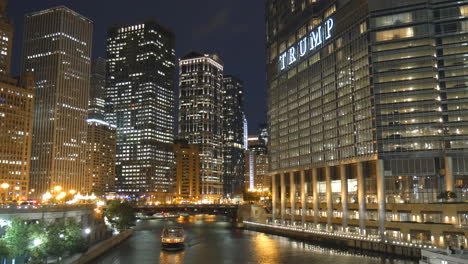 Chicago-riverwalk-view,-boat,-bridge,-skyscrapers,-towers,-night-and-evening-cityscape-scene,-trump-tower-illuminated