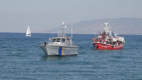 Wide-shot-of-a-boat-full-of-illegal-immigrants-from-the-Syrian-war-being-pulled-into-shore-by-the-coastguard-at-Latchi-Polis-Chrysochou,-Cyprus