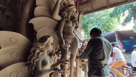 Poor-Indian-craftsman-making-clay-idol-of-Gods-and-Goddess-at-workshop-garage,-slow-camera-movement