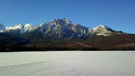 Vuelo-De-Drones-Sobre-Un-Lago-Congelado-Hacia-Una-Montaña-Cubierta-De-Nieve-En-Jasper,-Canadá