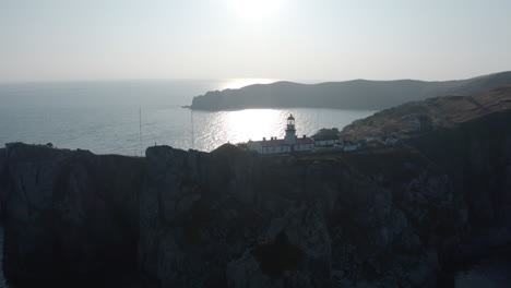 Slow-aerial-lift-up-shot-of-Gamov-lighthouse-building-complex,-standing-on-steep-rocky-cliff,-on-the-sunset